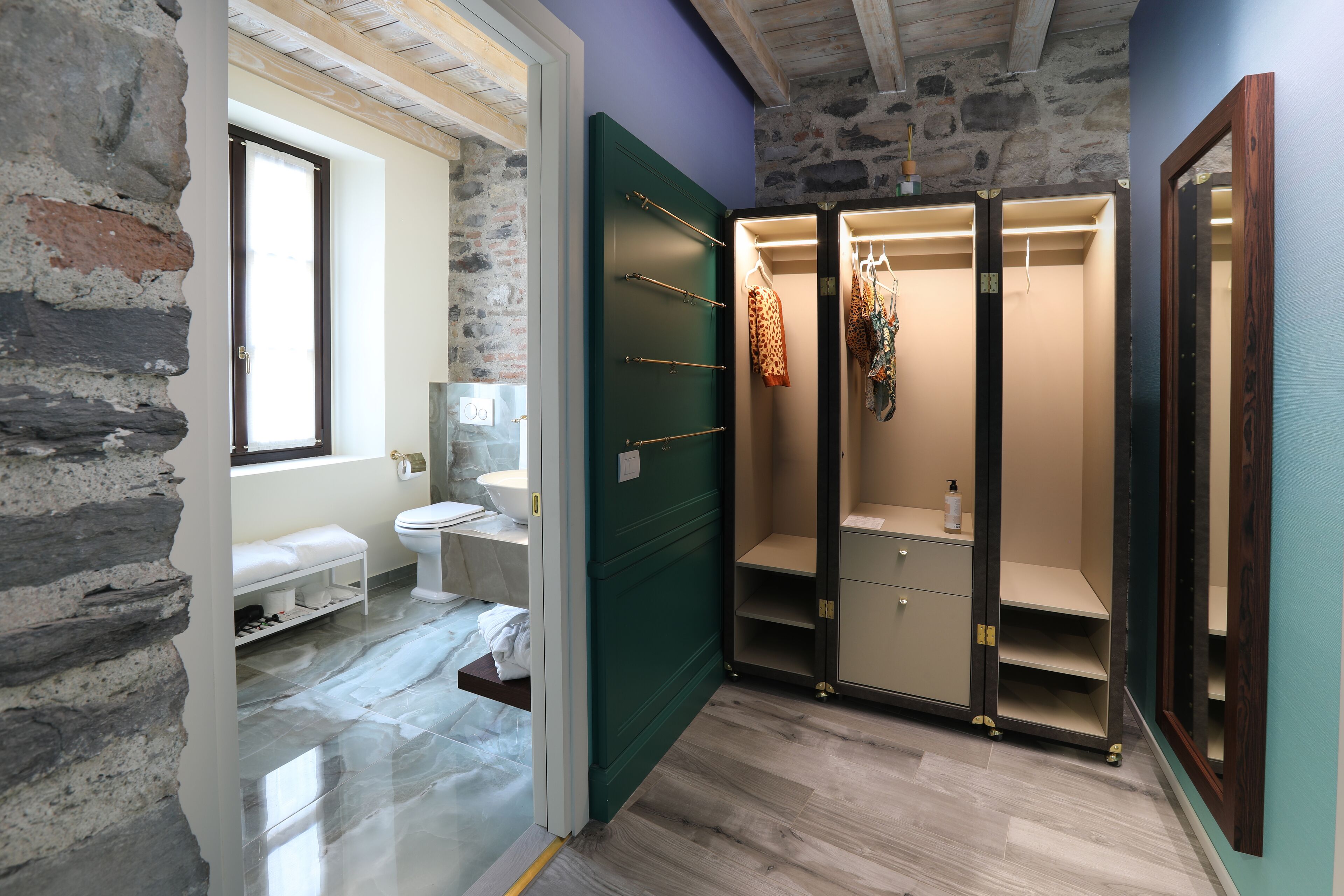 Un baño con pared de piedra, ventana, inodoro, lavabo y puerta verde.