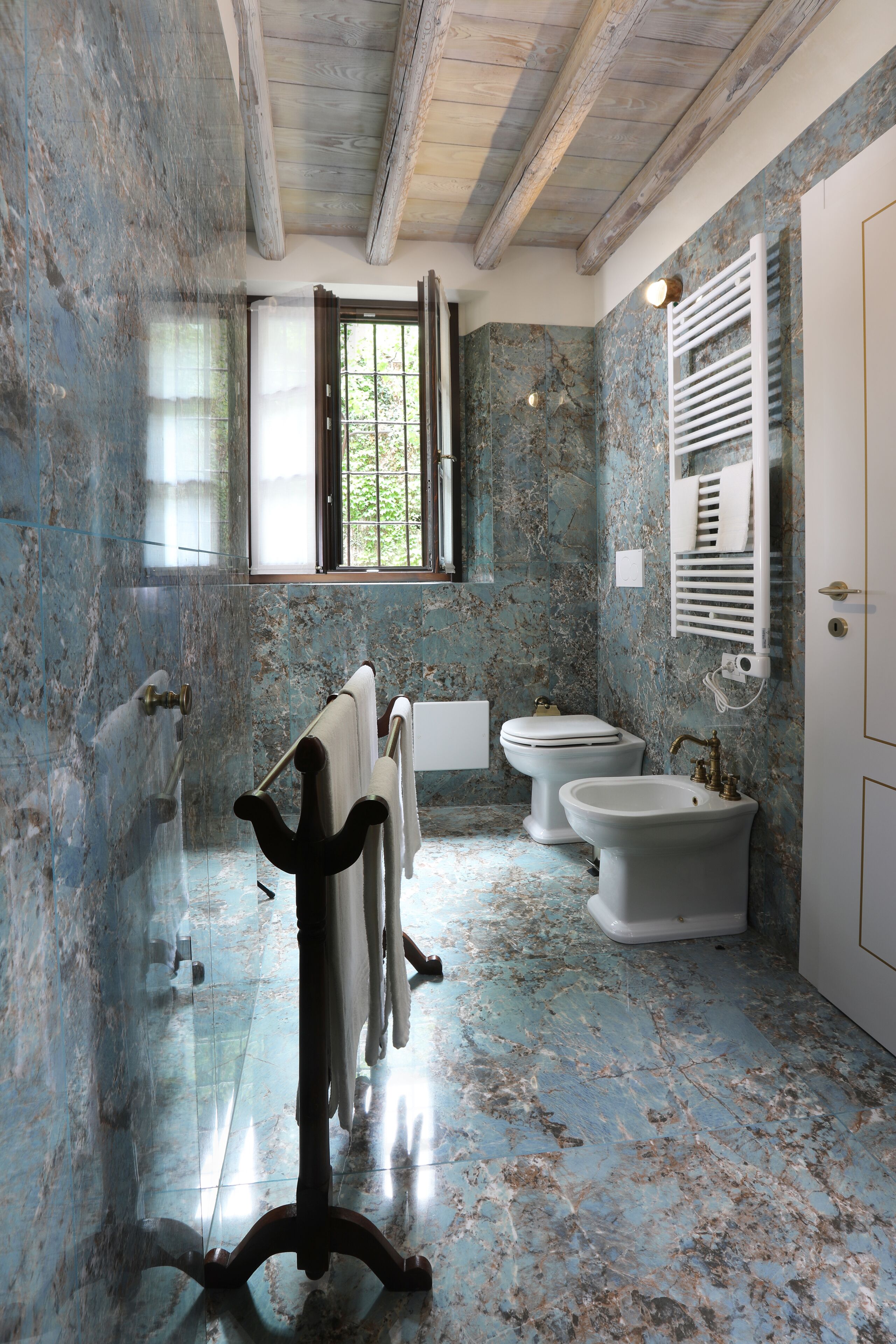 Un baño con paredes de mármol, una bañera, dos lavamanos y un ventanal con vistas al verdor.