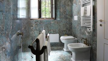 Un baño con paredes de mármol, una bañera, dos lavamanos y un ventanal con vistas al verdor.