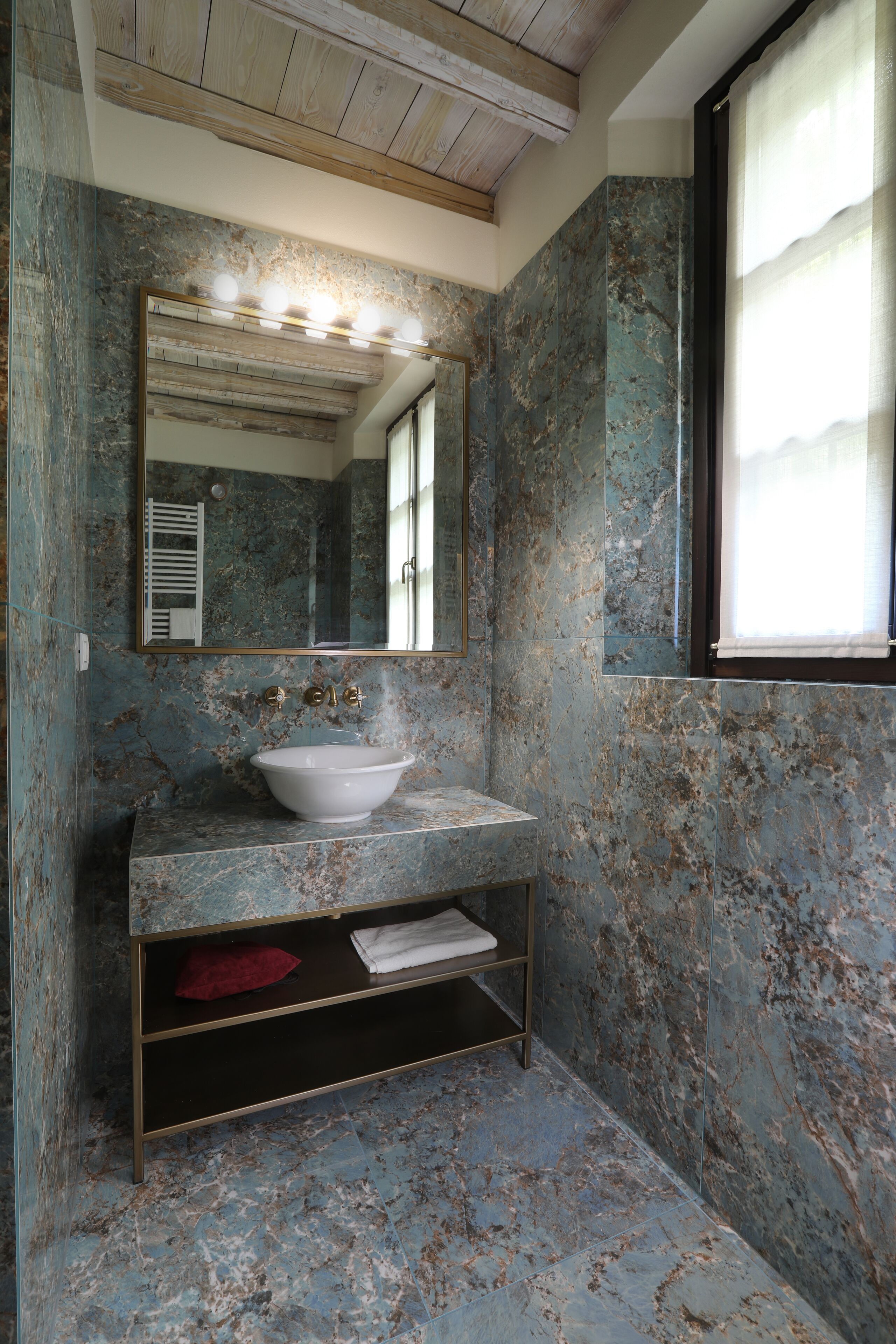 Un bagno con lavabo in marmo, uno specchio e uno scaffale.