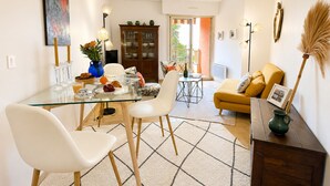 A modern living room with a glass dining table, white chairs, a yellow sofa, and a wooden cabinet. - l'Appartement Magnolia (Vallauris)