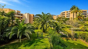 A hotel courtyard with palm trees, a green lawn, and buildings in the background. - l'Appartement Magnolia (Vallauris)