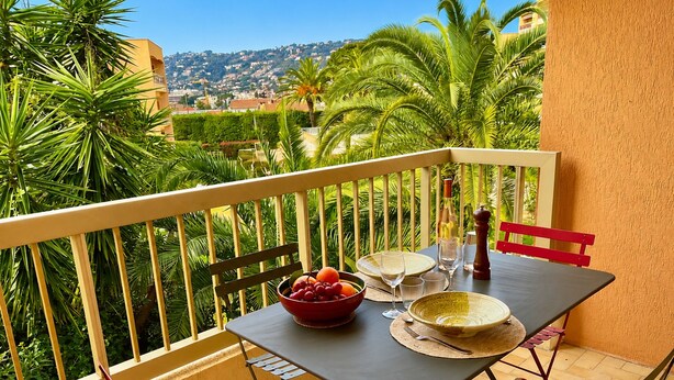 A balcony with a table set for two, a bowl of fruit, and a bottle of wine. - l'Appartement Magnolia (Vallauris)
