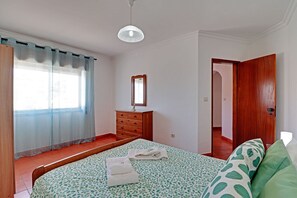 A bedroom with a bed, a wooden dresser, a mirror, and a door leading to another room.
