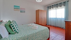 Una camera da letto con un letto, un armadio, una finestra con tende e due opere d'arte a parete.