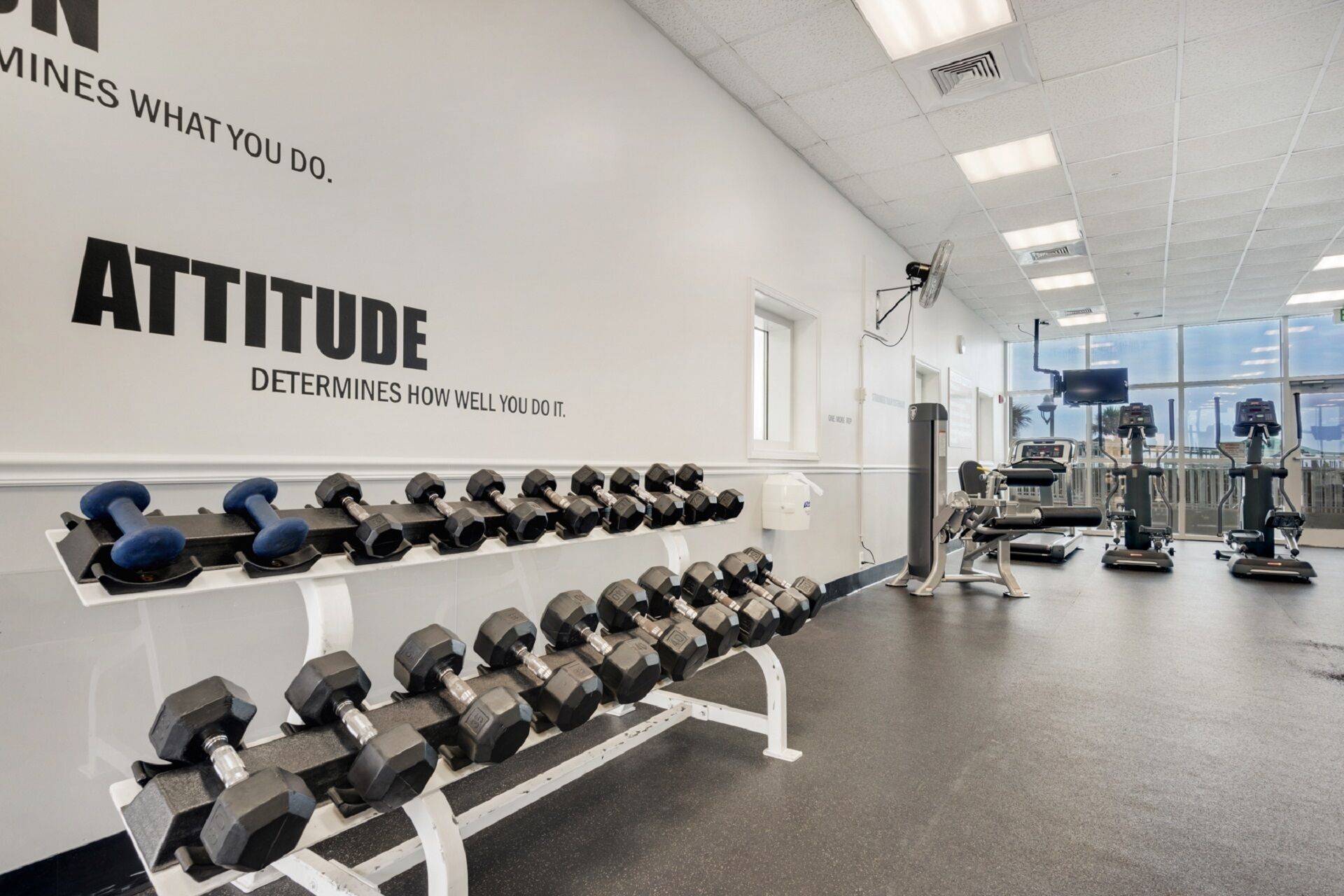 A gym with rows of dumbbells, exercise equipment, and motivational wall quotes.