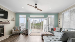 A spacious living room with a grey sofa, patterned armchair, and a ceiling fan. - 30A 5 Minute Walk to Beach / Private Heated Pool / View / Family Vacation (Santa Rosa Beach)