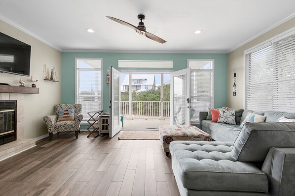 A spacious living room with a grey sofa, patterned armchair, and a ceiling fan.
