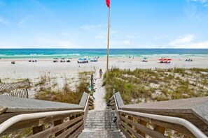 A beach view with a wooden staircase leading to the sand, a flagpole, and beach umbrellas.