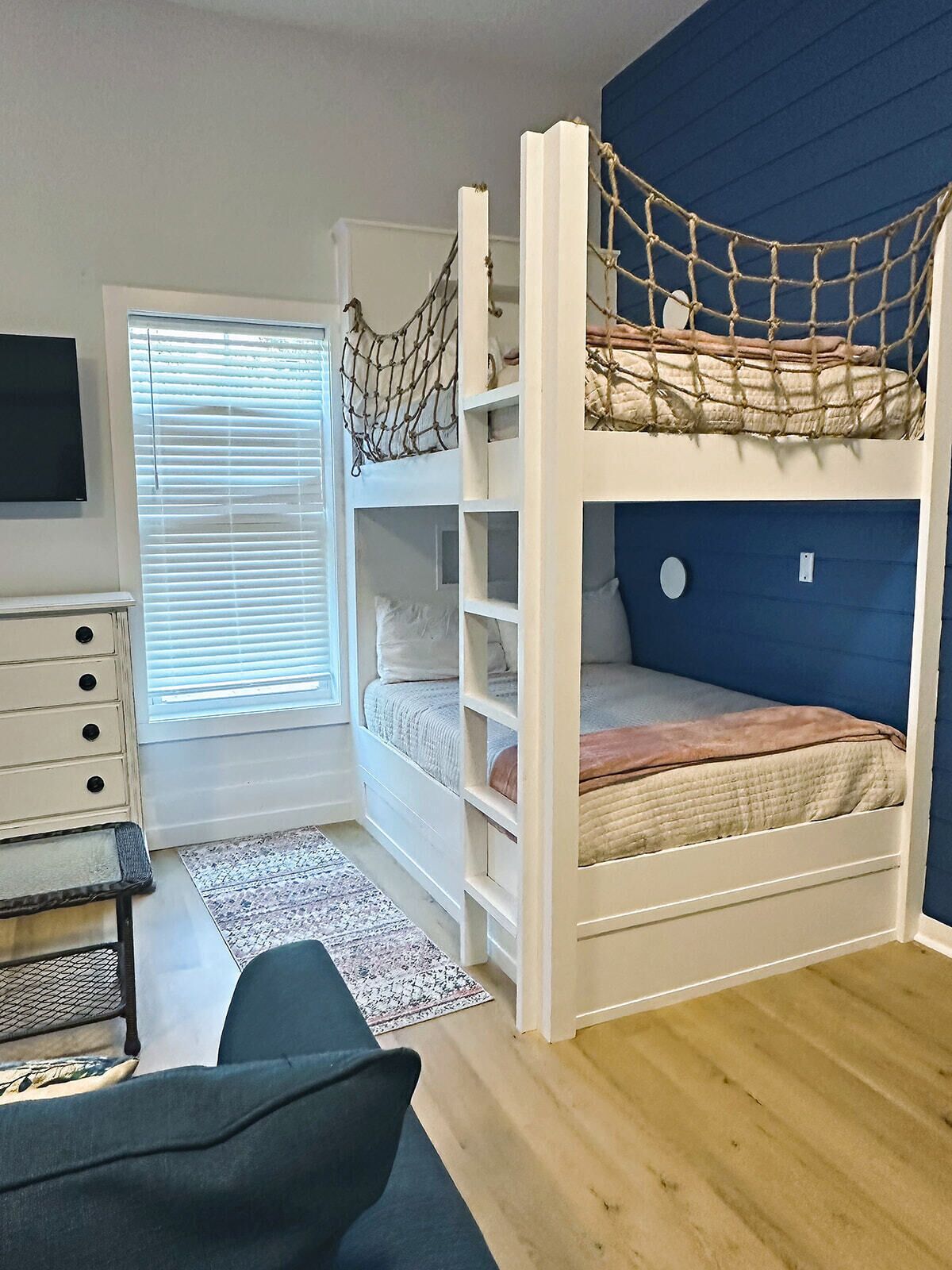 Un lit superposé avec un ciel de lit en forme de moustiquaire, une commode, un téléviseur et une fenêtre avec des stores.