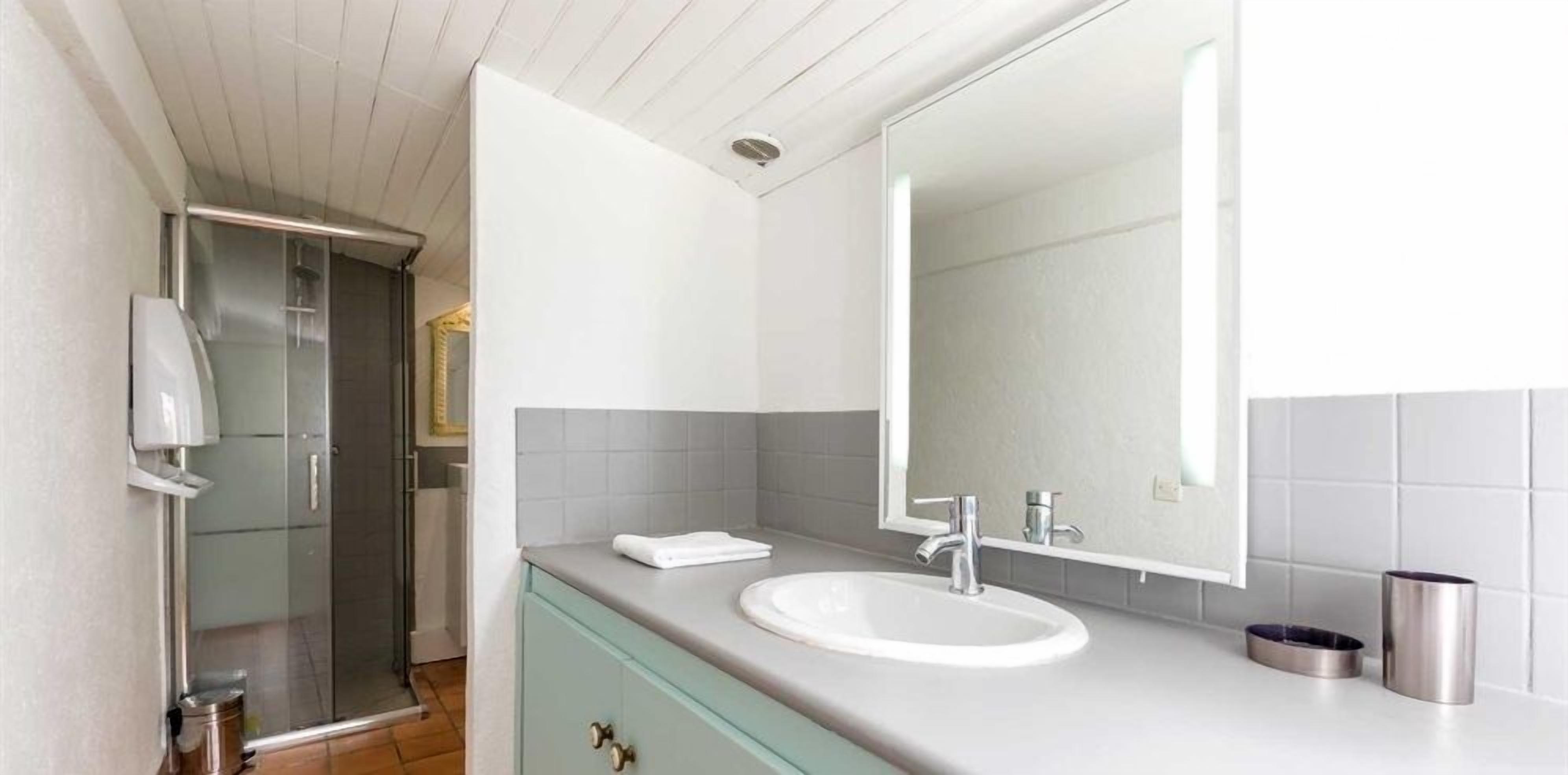 A modern bathroom with a white sink, a large mirror, and a shower area.