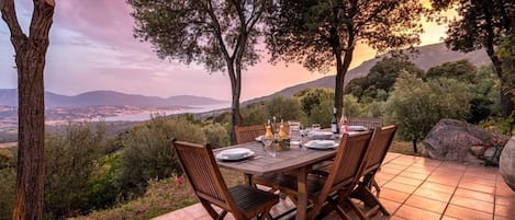 Una mesa de comedor al aire libre dispuesta en un patio con vistas panorámicas a un valle y montañas.