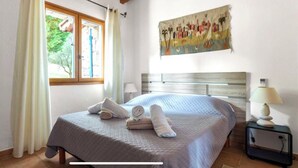 Un dormitorio con cama, mesita de noche, lámpara, ventana con cortinas y un cuadro en la pared.