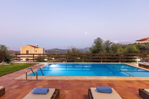 A rectangular swimming pool with a wooden deck, lounge chairs, and a view of the surrounding landscape.