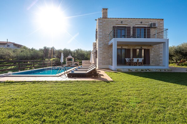 A modern house with a stone facade, a pool, and a patio with outdoor furniture.