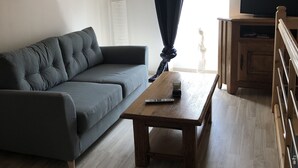Una sala de estar con un sofá gris, una mesa de centro de madera, un televisor sobre un mueble bajo y un aparador de madera.