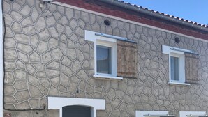 Un edificio de piedra con puerta negra, ventanas de marco blanco y techo rojo.
