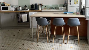 Una cocina moderna con una isla central, taburetes de bar y piso de baldosas.