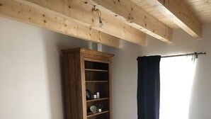 Un dormitorio con cama, vigas de techo de madera, una estantería empotrada y una ventana con cortina.