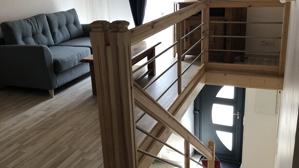 Una habitación tipo loft con una escalera de madera, un sofá gris y un televisor.