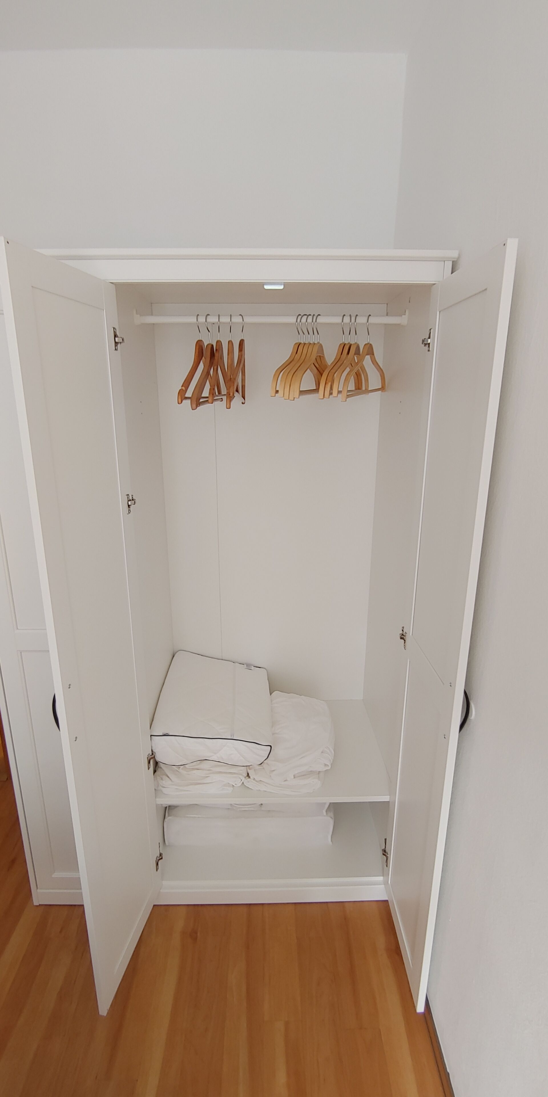 Un armari blanc amb penjalls de fusta i roba doblegada.