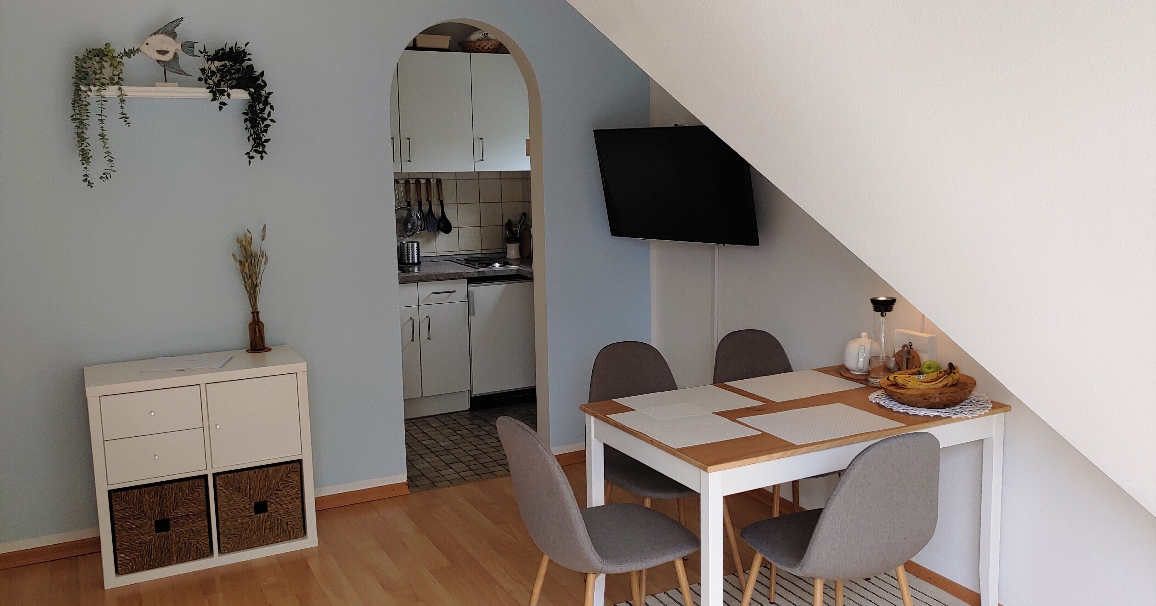 A compact kitchen with white cabinets, a hanging pot rack, and a dining area with a table and chairs.
