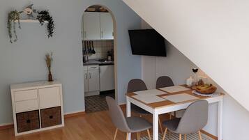 A compact kitchen with white cabinets, a hanging pot rack, and a dining area with a table and chairs.