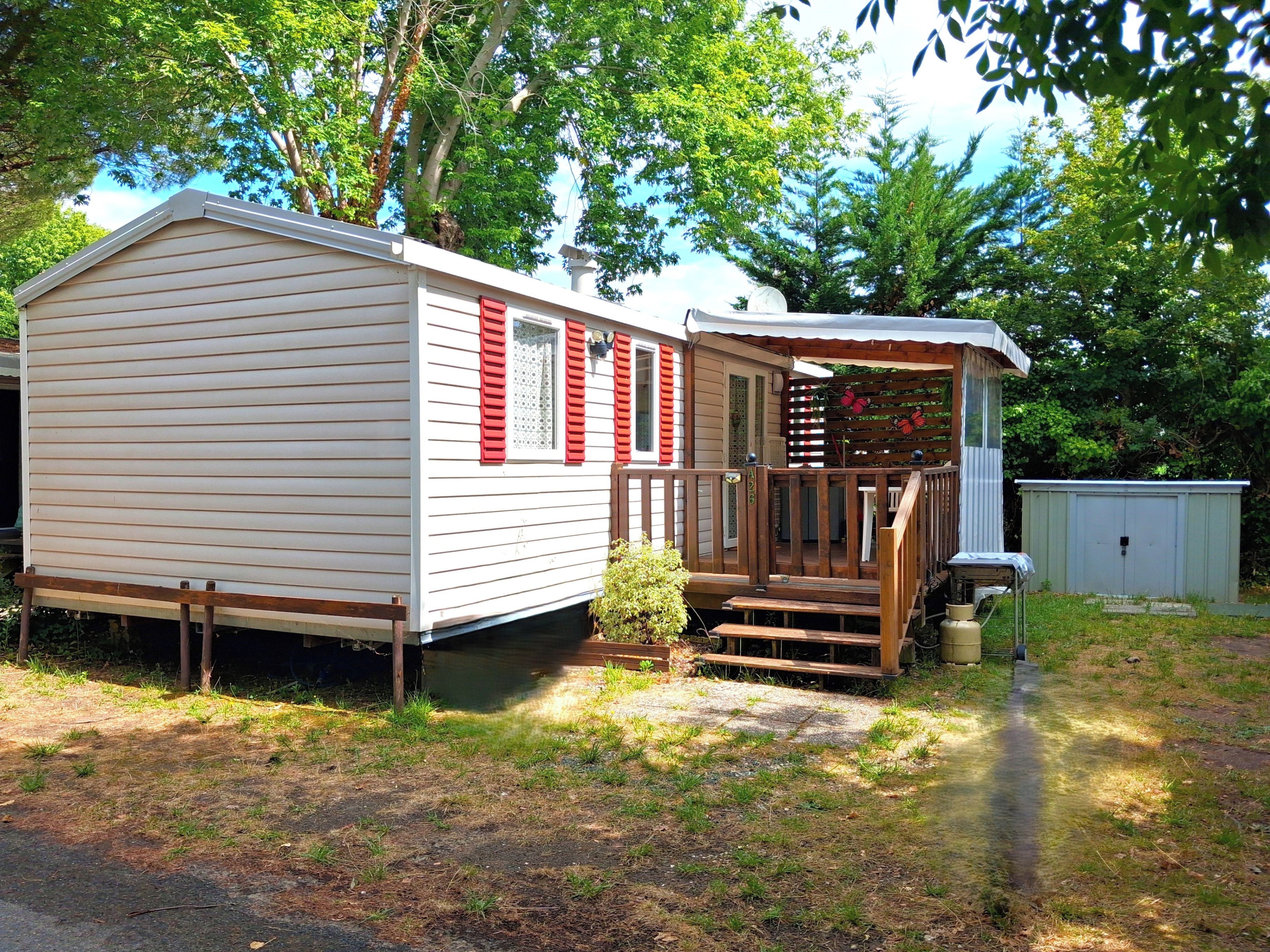 A mobile home with a porch, a small shed, and a garden area.