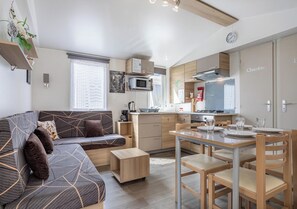 Un espacio habitable compacto con sofá, una mesa de comedor con sillas, kitchenette y microondas.