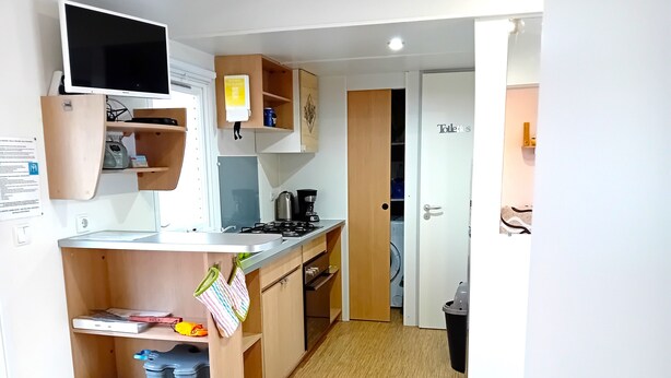 Une cuisine compacte équipée d’une cuisinière intégrée, d’une machine à café et d’un four à micro-ondes. On y trouve également une petite poubelle et un extincteur près de l’entrée.