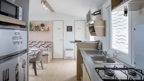 Een kleine keuken met een gasfornuis, een magnetron en een koelkast. Er is een zithoek met een bank en een stoel.
