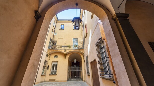 A narrow alleyway with a covered entrance, a wrought iron gate, and a building with balconies and windows. - UR-NEST d'Azeglio, Elegant one bedroom apartment (Bologna)