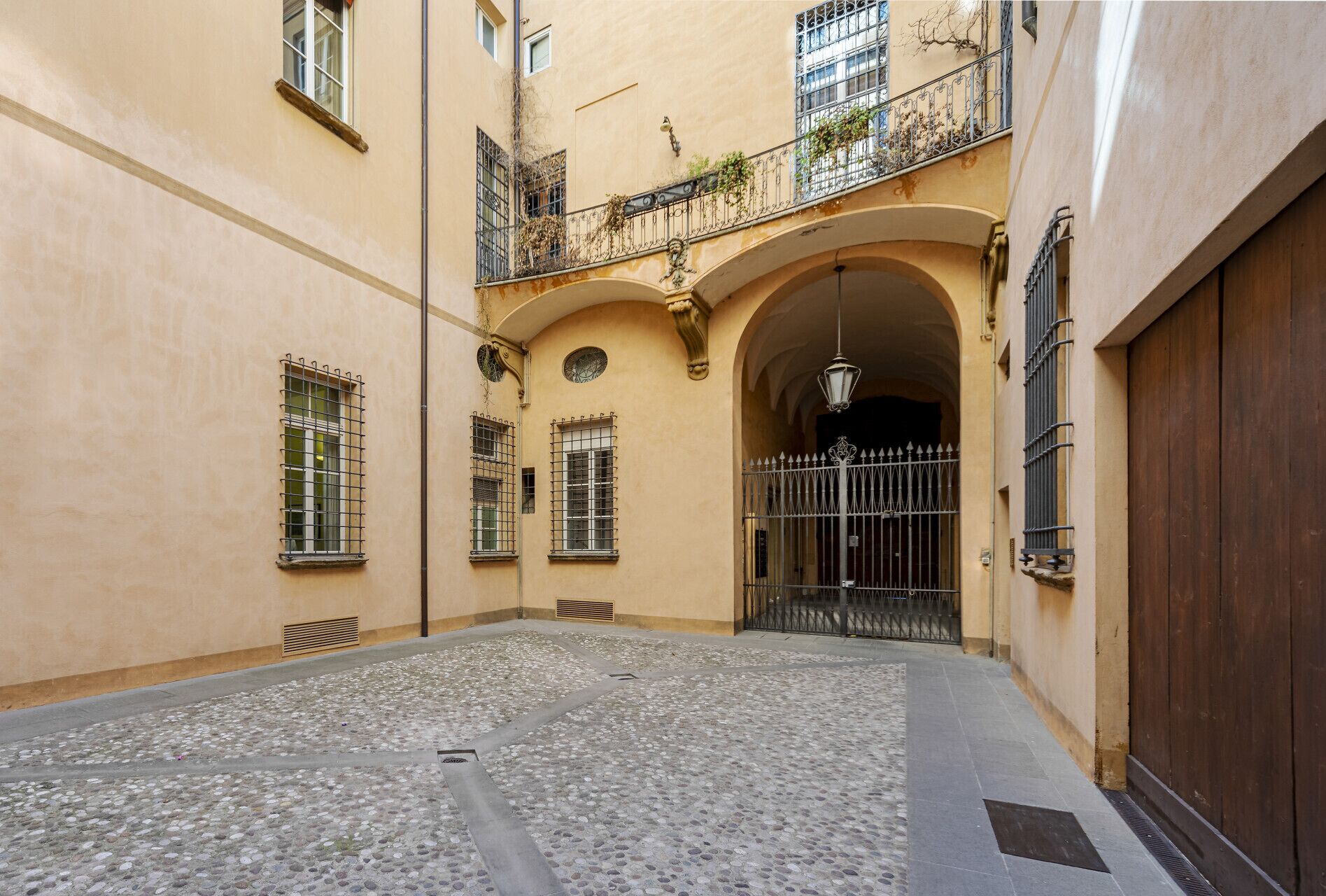 A courtyard with cobblestone flooring, a wooden door, and a metal gate.