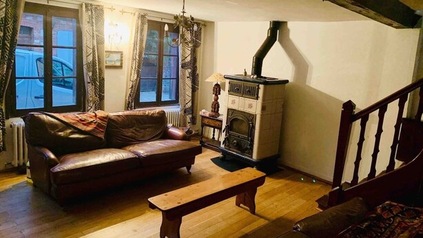 A cozy living room with a leather sofa, a wooden bench, a fireplace, and a staircase. - 16 century house in beautiful Norman village (Lyons-la-Forêt)