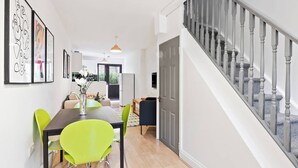 A modern kitchen with a dining area, a staircase, and a door leading to another room. - Beautifully Presented 2BD House, South East London (London)