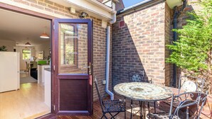 A patio with a round table and chairs, a wooden door, and a brick wall. - Beautifully Presented 2BD House, South East London (London)