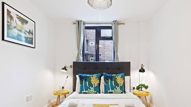 A bedroom with a large bed, two bedside tables, a window with curtains, and a framed picture on the wall. - Beautifully Presented 2BD House, South East London (London)