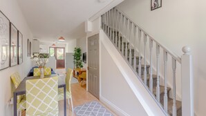 A modern kitchen with white cabinets, a dining area with yellow and white chairs, and a staircase with white railings. - Beautifully Presented 2BD House, South East London (London)