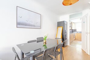A dining area with a table, chairs, and a framed picture on the wall.