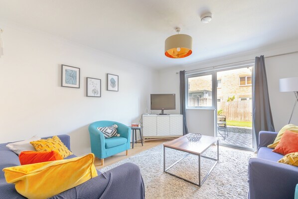 A modern living room with a sofa, armchair, coffee table, and artwork on the wall.