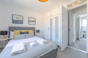 A neatly made bed with pillows and towels, a bedside lamp, and a wall with two framed pictures.