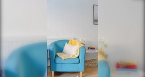 A room with a blue armchair, a small side table with books, and a white wall. - Stylish 4BD Home with Garden Near Kennington (London)