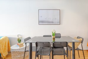 A dining area with a rectangular table, six chairs, a vase with flowers, and a framed picture on the wall.