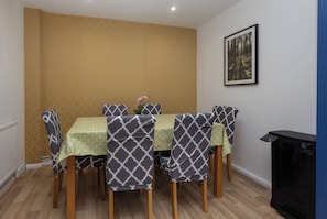 A dining area with a table set for four, surrounded by patterned chairs, a vase with flowers, and a framed picture on the wall.