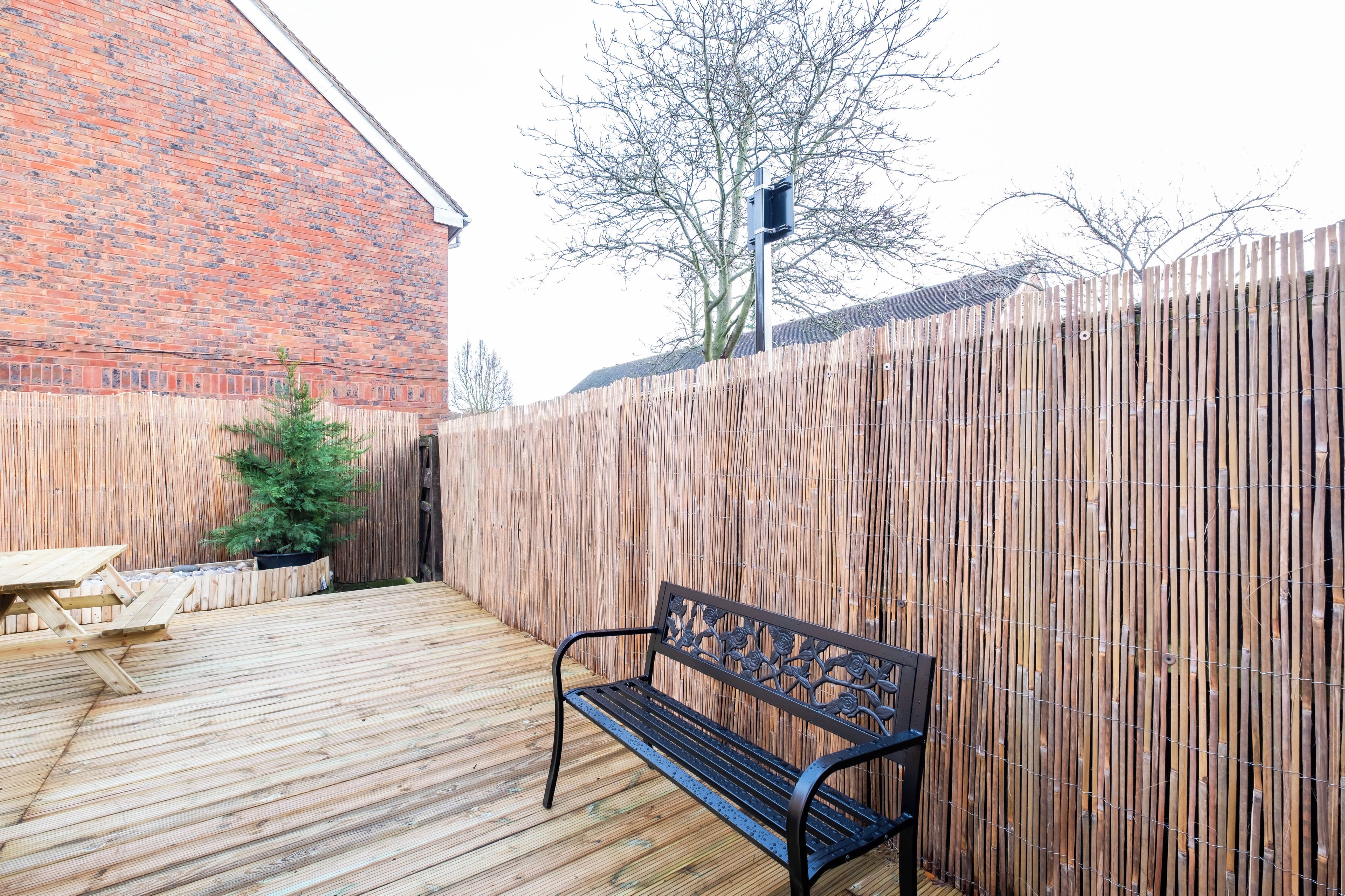 A wooden deck with a bench and a picnic table, surrounded by a bamboo fence.