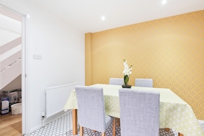 Un coin repas avec une table dressée pour quatre personnes, des chaises et un vase rempli de fleurs blanches.