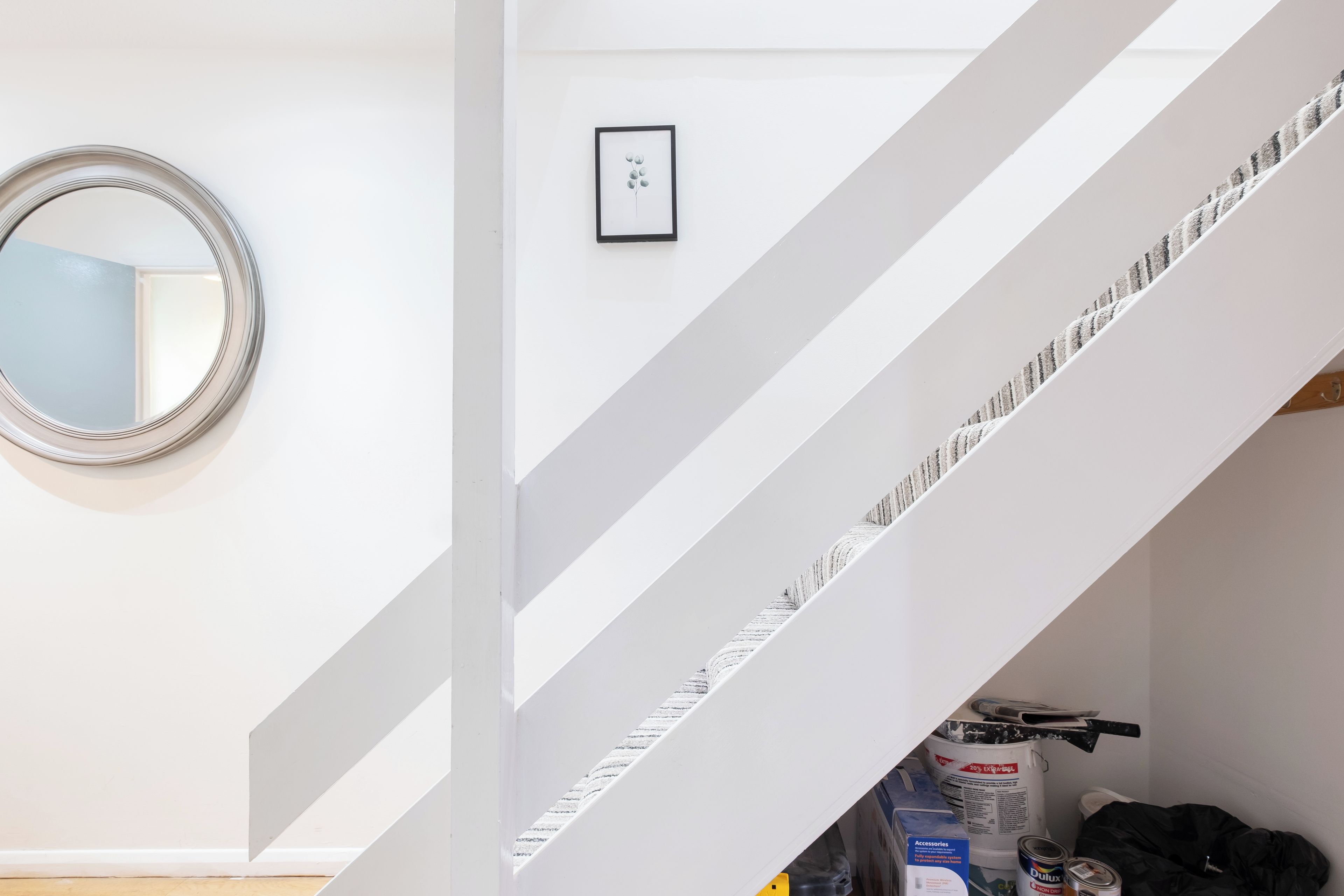 A staircase with a white railing, a round mirror on the wall, and a small framed picture.