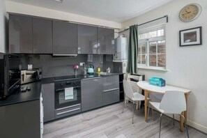 A modern kitchen with dark cabinets, a built-in oven, and a dining area with a table and chairs.