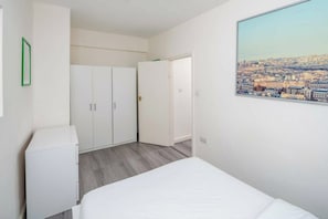 A bedroom with a bed, a wardrobe, a door leading to another room, and a cityscape view. - Modern 2BDR City Retreat Angel & Shoreditch Border (London)
