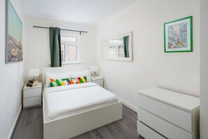 A bedroom with a bed, bedside tables, a dresser, a window with curtains, and a framed picture on the wall.